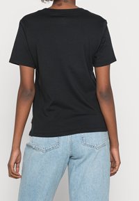 Camiseta de algodón negra de manga corta y cuello redondo, mostrada desde la espalda, con un corte relajado y una etiqueta en la costura lateral.