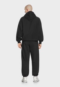 Czarny zestaw bluz i spodni dresowych, wykonany z miękkiego materiału. Posiada kaptur, opadające ramiona i elastyczne mankiety. Slim fit o prostym designie.