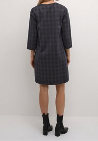 Abito a quadri navy con maniche a tre quarti, scollatura rotonda e orlo leggermente svasato. Indossato con stivali neri alla caviglia.