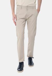 Pantaloni leggeri beige con taglio dritto. Presentano una chiusura con bottone e tasche laterali. Abbinati a sneaker nere e una camicia neutra.