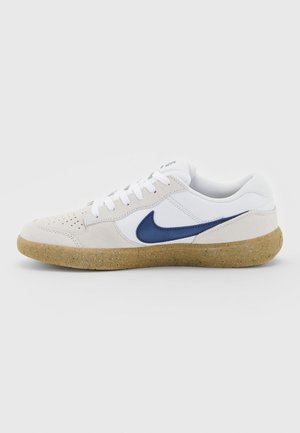 Witte sneakers met een marineblauwe Nike-logo, vervaardigd uit suede en mesh, perforierte tenen en een getextureerde gumrubberen zool. Zijaanzicht.