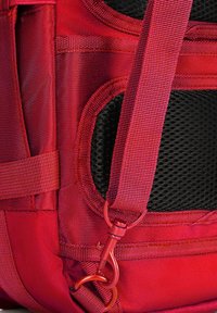 Červený látkový batoh se síťovanou částí, nastavitelné popruhy a kovovou sponou. Disponuje texturovaným povrchem a zesíleným švem.
