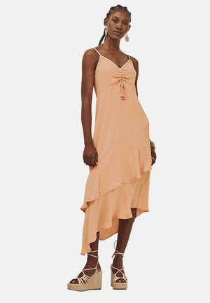 Vestido midi melocotón con tirantes de espagueti ajustables, detalle fruncido en el frontal y dobladillo asimétrico con volantes. Combinado con cuñas de esparto color tostado.