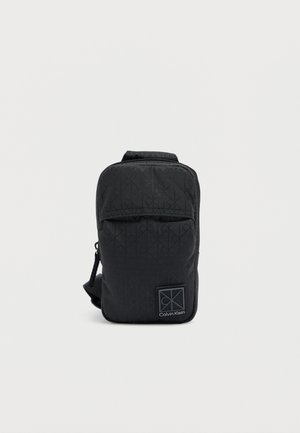Black nylon bag with a geometric pattern, a top zipper closure, and a front logo patch. Features an adjustable strap for easy carrying.