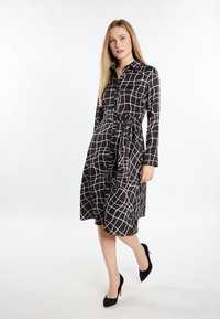 Mustavalkoinen ruudullinen mekko, jossa on pitkät hihat, kapeat vyötärö ja napit edessä, sekä polvipituinen hameosa. Asusteena mustat korkokengät.