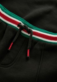 Black joggers with a textured fabric, featuring a green, red, and white striped waistband and drawstring accents.