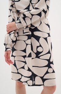 Long-sleeve dress featuring a cream base with bold black abstract shapes, gathered cuffs, and a smooth, textured fabric finish.