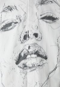 Gestreifter Stoff in Schwarz und Weiß mit einer Linienezeichnung eines Gesichts, das die Gesichtszüge mit einem texturierten, grafischen Design betont.