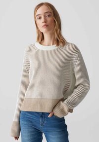 Gestrickter Pullover mit einem gestreiften Design in hellem Creme und Braun, mit geripptem Textur, Rundhalsausschnitt und lockerer Passform, kombiniert mit blauen Jeans.