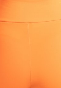 Leggings met hoge taille, nauwsluitend, gemaakt van feloranje stof met een gladde textuur en minimale naden. Geen opvallende patronen of bevestigingen.