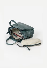 Teal leren rugzak met een ritssluiting bovenaan, voorzien van een gestreepte binnenkant, meerdere zakken en een klein beige etui. Glad van textuur, minimalistisch ontwerp.