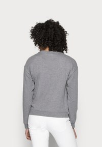 Grå sweatshirt med en avslappnad passform, mjuk textur, sänkta axlar och ribbade ärmmuddar och nederkant. Bärs med vita jeans.