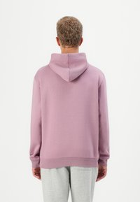 Pink hooded sweatshirt with a soft texture, ribbed cuffs, and hem. Back view, worn with light gray sweatpants. Simple design, no patterns.