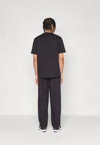 Sort bomulds t-shirt og løstsiddende bukser. T-shirten har korte ærmer, og bukserne er lange og afslappede. Begge dele er i ensfarvet sort.