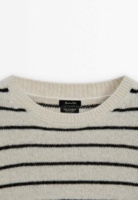 Cremfarbener Kaschmirsweater mit schwarzen horizontalen Streifen, mit einem runden Ausschnitt und weicher Textur. Das Etikett trägt die Aufschrift "100% Kaschmir."