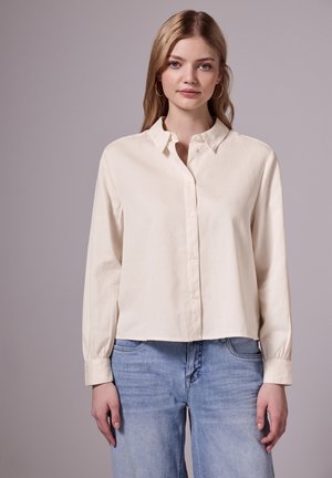Crème kleurig, lang mouw overhemd met knopen en een kraag, ontspannen pasvorm en subtiele textuur, gecombineerd met lichtblauwe jeans.