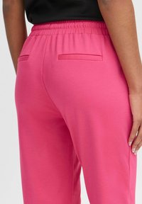 Rosa Sweatpants mit einem elastischen Bund, ausgestattet mit zwei Gesäßtaschen, einem glatten Textur und einem lockeren Schnitt für zusätzlichen Komfort.