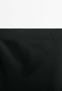 Sort stof med en glat tekstur, foldet i bunden, mod en skarp hvid baggrund. Designet er minimalistisk og monokromatisk.
