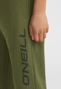 Grüne Jogginghose aus Baumwolle mit lockerer Passform, die ein schwarzes Logo auf der Seite aufweist. Der Stoff wirkt glatt mit einem leichten Glanz.