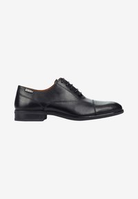 Zapato de vestir de hombre en cuero negro con puntera de pala, cierre con cordones, tacón bajo y una pequeña etiqueta de marca cerca del tobillo sobre un fondo blanco.