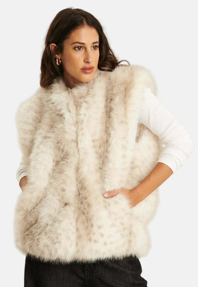 Faux bont vest in licht beige met een zachte textuur, voorzien van een coltruim ontwerp en twee zijzakken. Draag het over een witte lange mouwen shirt.