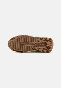 Suela de zapato con textura estriada, hecha de un material de goma color topo. "MICHAEL KORS" estampado en el centro, rodeado por un marco rectangular.