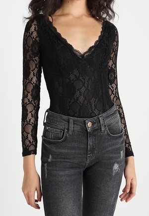 Sort blondette bodysuit med lange ærmer og en dyb V-udskæring. Mønsteret har florale motiver. Sammen med slidte sorte højtaljede jeans.