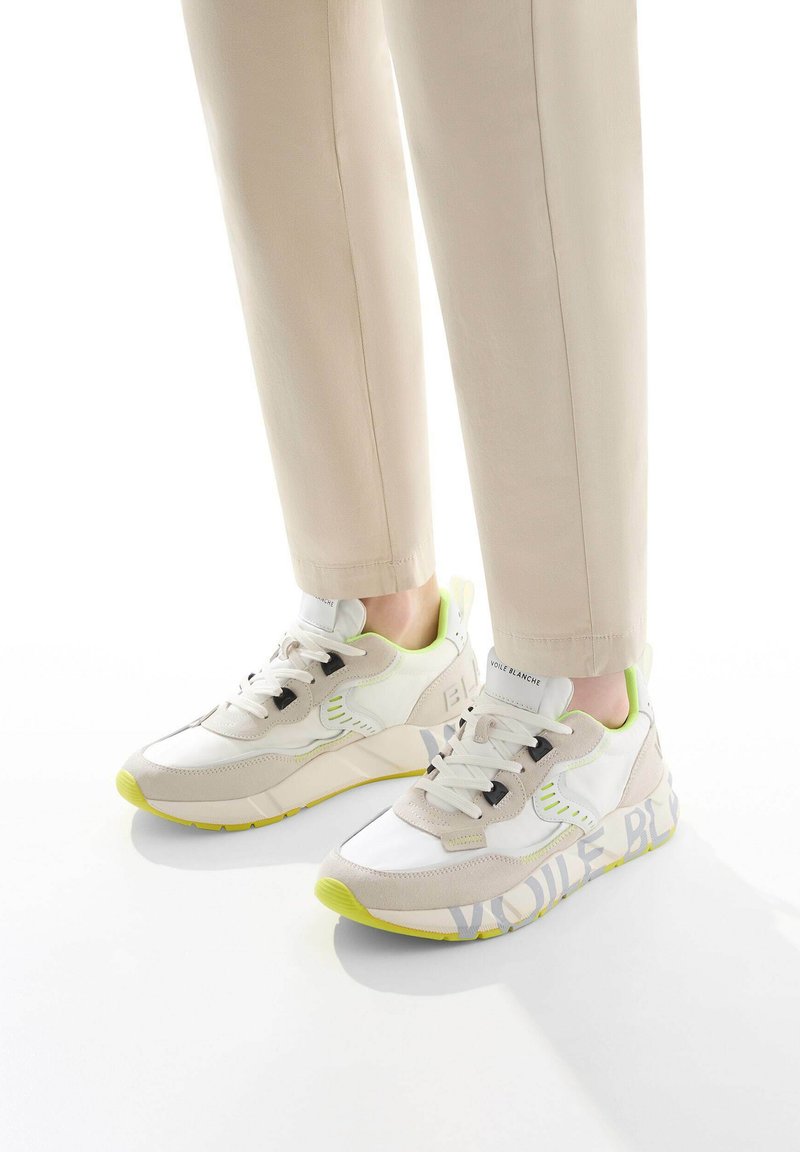 Zapatillas deportivas en beige, blanco y verde neón, que presentan una combinación de materiales suaves y texturizados con detalles del logo en el lateral.