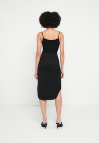 Fekete, testhezálló ujjatlan felső vékony pántokkal, fekete, középhosszú szoknyával, oldalhasítékkal és sima textúrával párosítva.