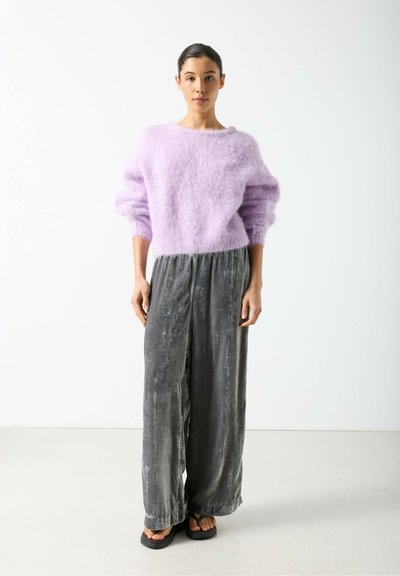 Pull moelleux lilas à manches larges associé à un pantalon large en velours gris, avec une taille légèrement froncée. Sandales plates noires.