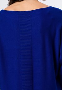 Niebieski sweter z dzianiny z szerokim dekoltem i ribbowym pionowym detalem z tyłu, kontrastującym z gładką teksturą materiału.