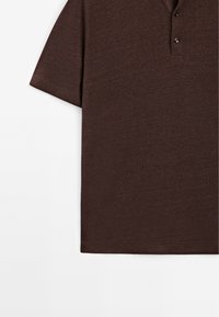 Polo shirt marrone a maniche corte con tessuto testurizzato, patta con tre bottoni e dettagli di cucitura sottili vicino all'orlo e alle maniche.