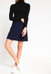 Pull en col roulé noir associé à une jupe évasée bleu marine et des baskets blanches, mettant en avant une texture lisse et un design simple.