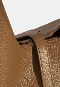 Bruine leren tas met een gestructureerd oppervlak, voorzien van een brede schouderriem en zichtbare stiksels op de randen. Het sluitontwerp is gestroomlijnd.