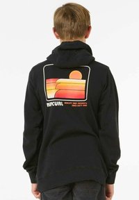 Hoodie noir avec un graphique rétro de coucher de soleil coloré au dos, contenant le texte "Ripcurl" et des lignes courbes en orange et jaune.