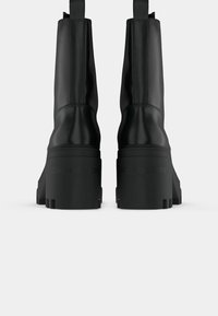 Black leather platform boots shown from the back, with thick soles and "Calvin Klein Jeans" embossed on the heel.