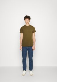 Tricou din bumbac de culoare verde măsliniu, cu decolteu rotund și buzunar pe piept, asortat cu blugi skinny albaștri și adidași albi. Design simplu și casual.