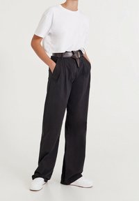 Czarne, szerokie spodnie z kantami, zestawione z białą koszulką z krótkim rękawem. Outfit dopełnia ciemny pasek i białe trampki.