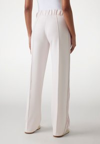 Pantalons de sport rose clair avec une coupe à jambes larges et une taille élastique. Présente des rayures latérales de couleurs contrastées et une texture de tissu lisse.