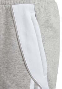 Pantalones deportivos grises con un panel lateral blanco, fabricados en tejido suave con un acabado ligeramente texturizado y detalles de costura en un gris contrastante.