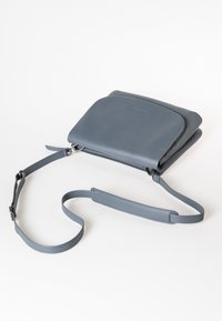 Graue Leder-Crossbody-Tasche mit rundem Klappdeckel, Reißverschluss und verstellbarem Tragegurt, mit glatter Textur und minimalistischer Design.