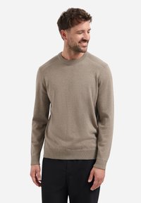 Lichtbruine gebreide trui met een ronde hals. Het heeft geribbelde accenten op de schouders en manchetten. Gepaard met donkere broek. Zachte textuur.