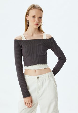 Dunkelgraues geripptes Langarm-Crop-Top mit schulterfreiem Design und weißem Rüschensaum. Kombiniert mit hellen, locker sitzenden Hosen.