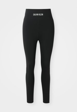 Leggings neri a vita alta di Calvin Klein, con vestibilità slim e logo stampato in bianco sulla cintura, esposti su uno sfondo neutro.