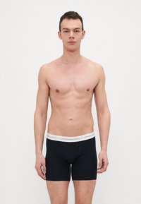 Čierne boxerky s bielym elastickým pásom so textom "Copenhagen Studios". Tkanina vyzerá hladko a priliehavo.
