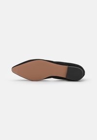 Sapato preto em camurça com biqueira em ponta, sola lisa em tom de tan e um pequeno salto texturizado em preto, apresentando um design minimalista.