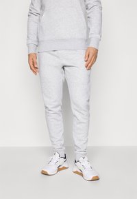 Gray sweatpants with a tapered fit and elastic cuffs, paired with white athletic shoes featuring a gum sole and black accents.