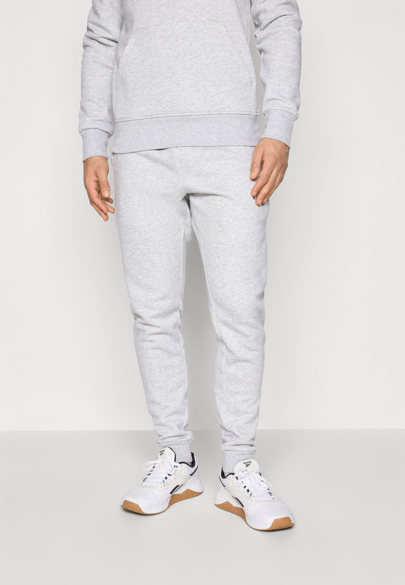 Gray sweatpants with a tapered fit and elastic cuffs, paired with white athletic shoes featuring a gum sole and black accents.
