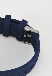 Bracelet de montre en silicone bleu marine avec une surface texturée, présentant une boucle en métal argenté et des trous de réglage pour la taille.