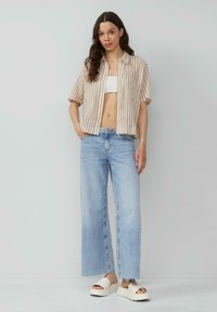 Gestreepte beige en crèmekleurige kortemouwen shirt, witte crop top, lichtblauwe wijde jeans en chunky witte instapsandalen.